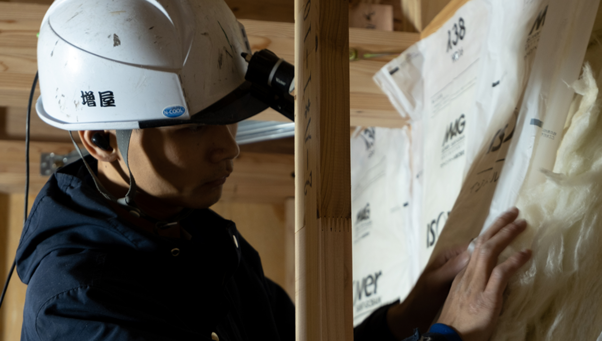 建設現場でヘルメットを着用し、木材と断熱材の施工を行う作業員の様子